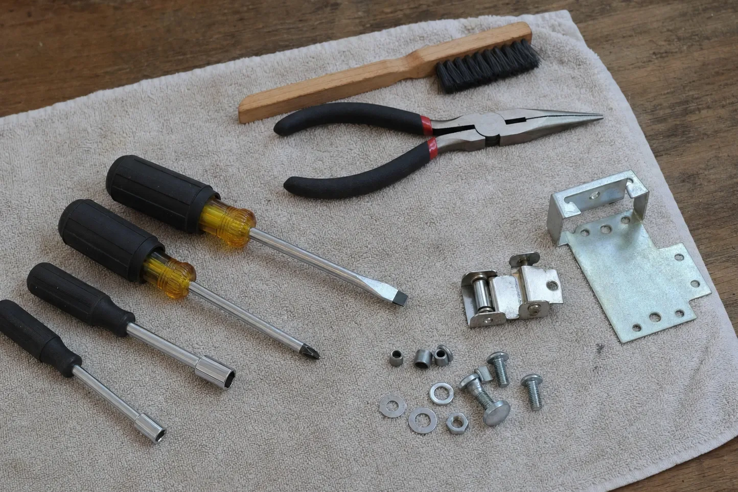Refrigerator door hinge with its roller and a galvanised bracket beside nut drivers and pliers on a towel