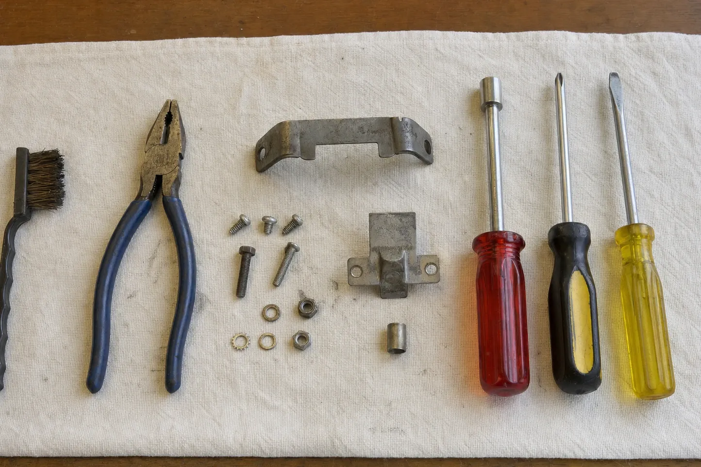 A long sheet-metal mounting bracket and a tabbed cover bracket with screws, nuts and a spacer sleeve on canvas
